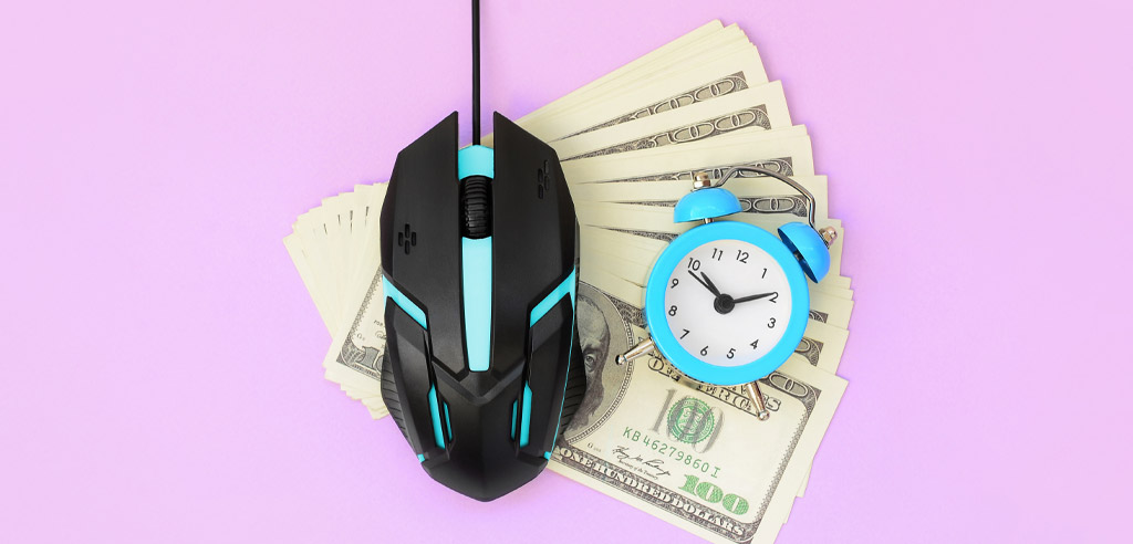 Computer mouse and a clock resting on a fanned-out pile of hundred dollar bills