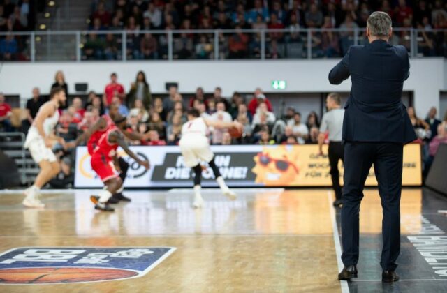 Professional basketball coach at an indoor basketball court supervising players in a game