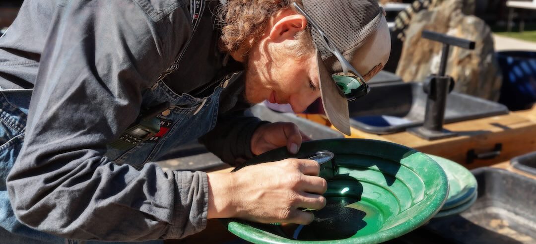 Man examining gold he has panned with a magnifying glass.