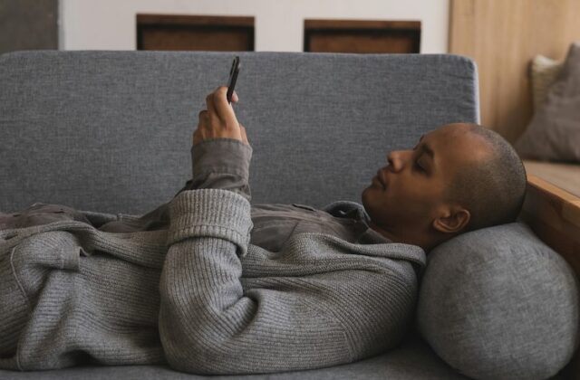 Man lying on couch completing Qmee microtasks on his phone.