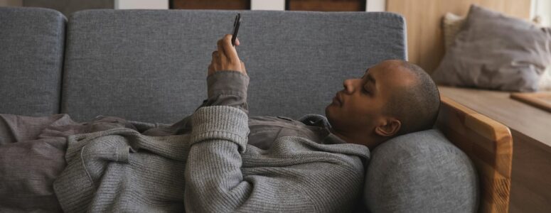 Man lying on couch completing Qmee microtasks on his phone.