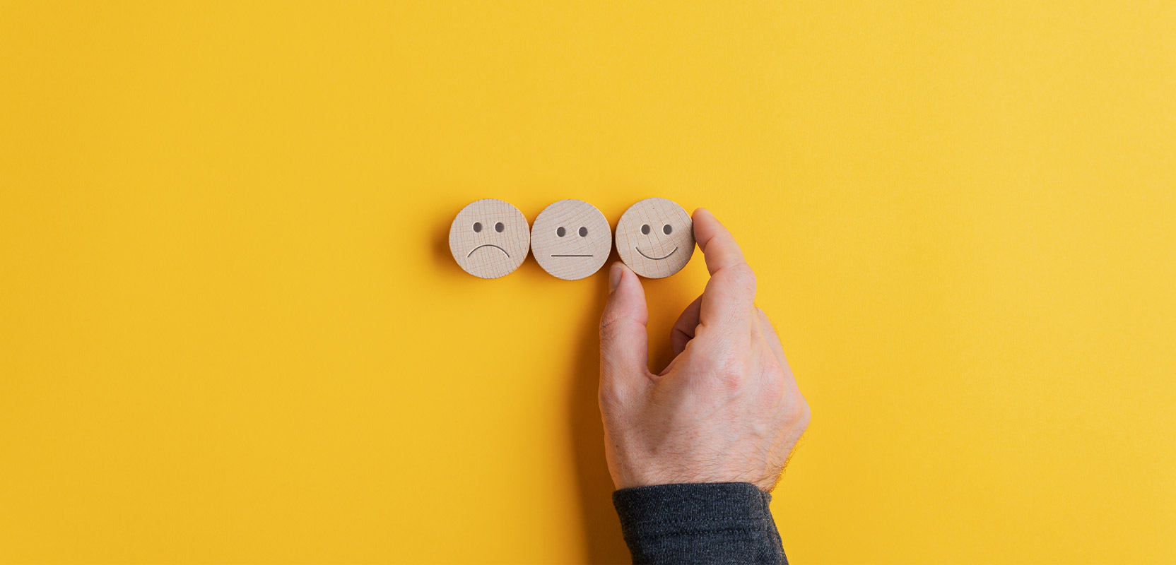 Three wooden blocks in the shape of faces with unhappy, neutral, and happy expressions, representing reviewing as an online side hustle