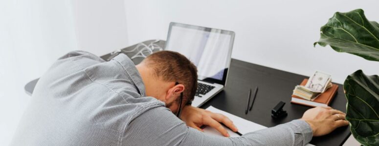 A frustrated employee who experiences quiet firing resting their head on the desk.
