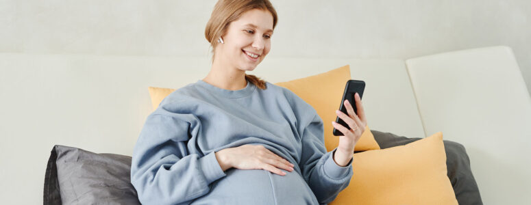 Pregnant mom sitting in bed working on a side hustle on her phone.