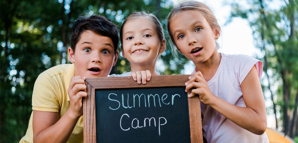 Three children gathered around a sign for summer camp