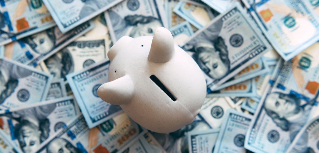 Piggy bank sitting on a pile of hundred dollar bills