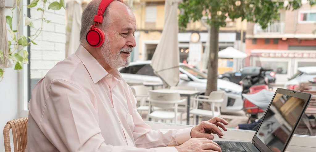 Older man wearing headphones and typing at a laptop as part of his freelance transcription side hustle