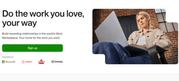 Upwork.com website homepage, showing a signup button next to an image of a digital freelancer sitting and typing on a laptop