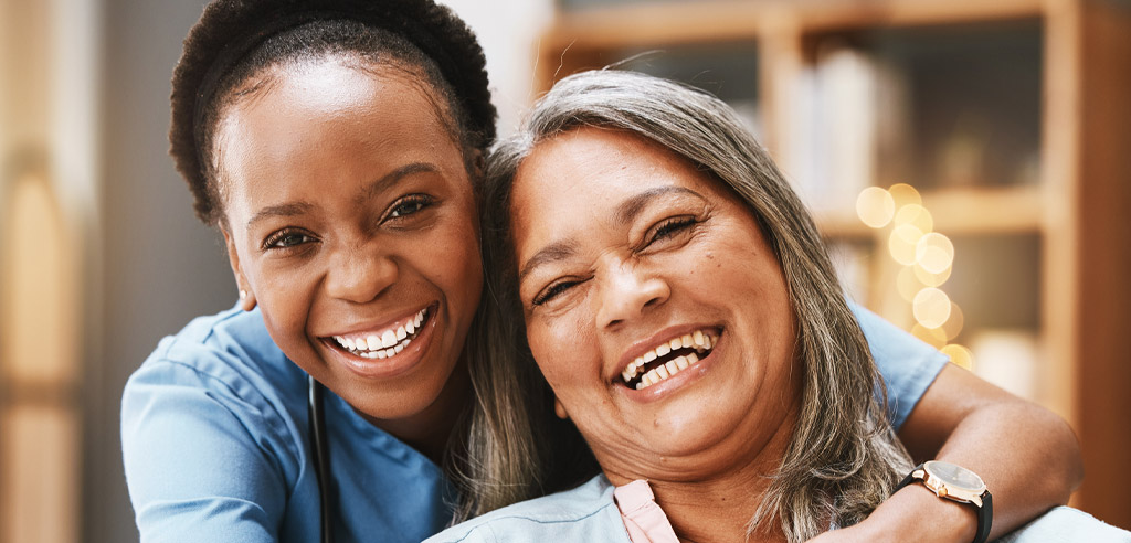 Female caregiver hugging an older woman and smiling