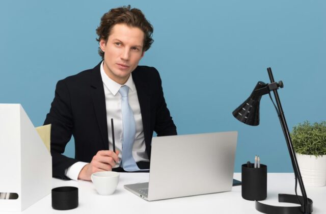 Professional consultant in a suit looking thoughtful and sitting at a white desk with a laptop and mug