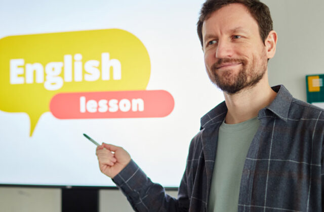 ESL teacher smiling and pointing to a screen that says "English lesson"