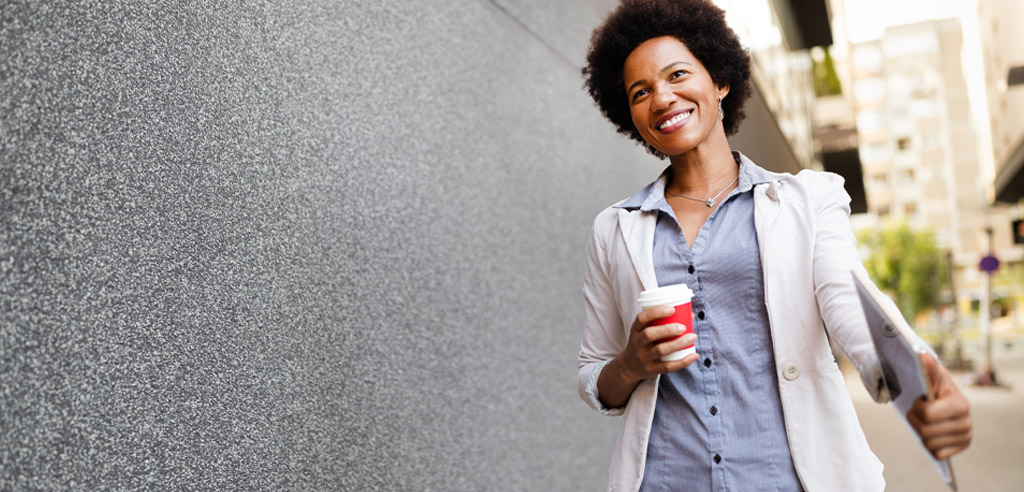 Woman walking outside holding a cup of coffee and considering her mobile notary side hustle