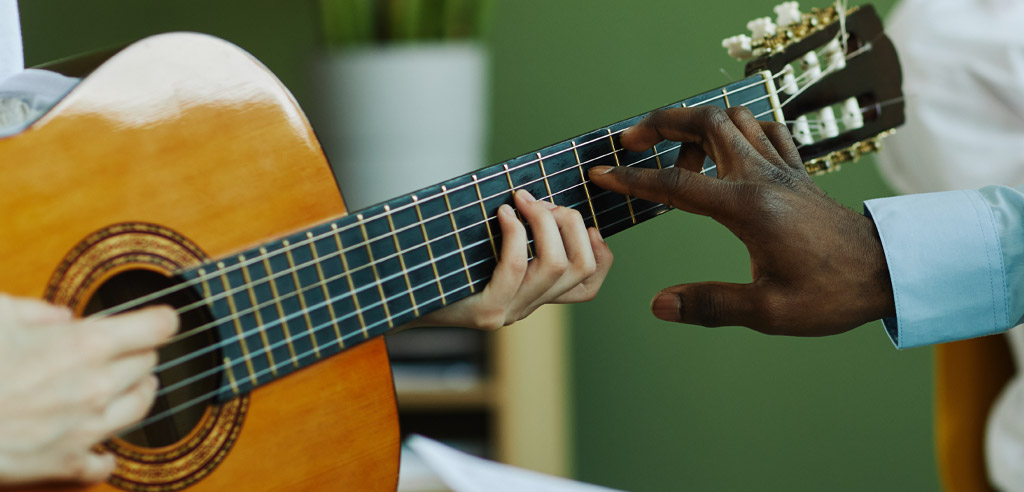 Music teacher showing a student where to place their fingers on a guitar.