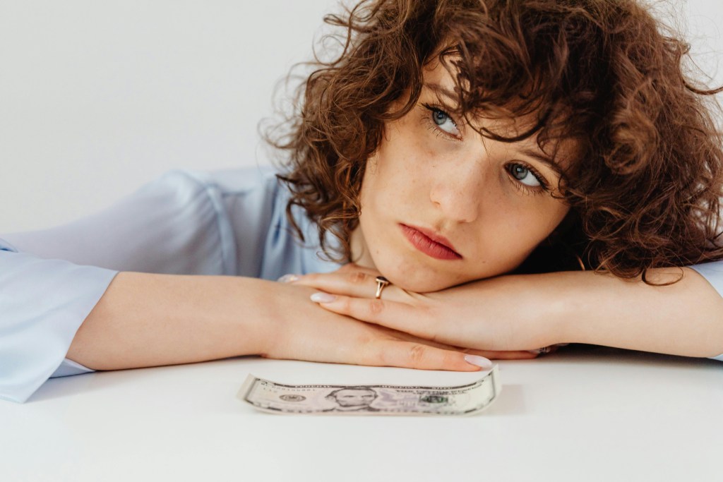 Woman in debt wondering how to spend single bill on the table.