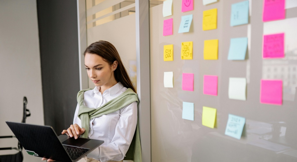 An overwhelmed worker standing in front of a bulletin board full of sticky notes with extra tasks.